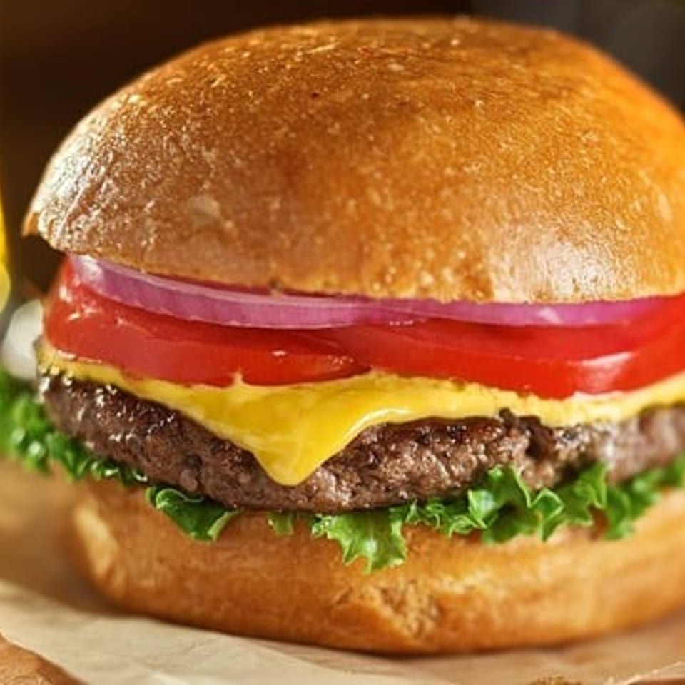 Cheeseburger on a wooden board with lettuce, beef patty, melted cheese, tomato, red onion, and a toasted bun.