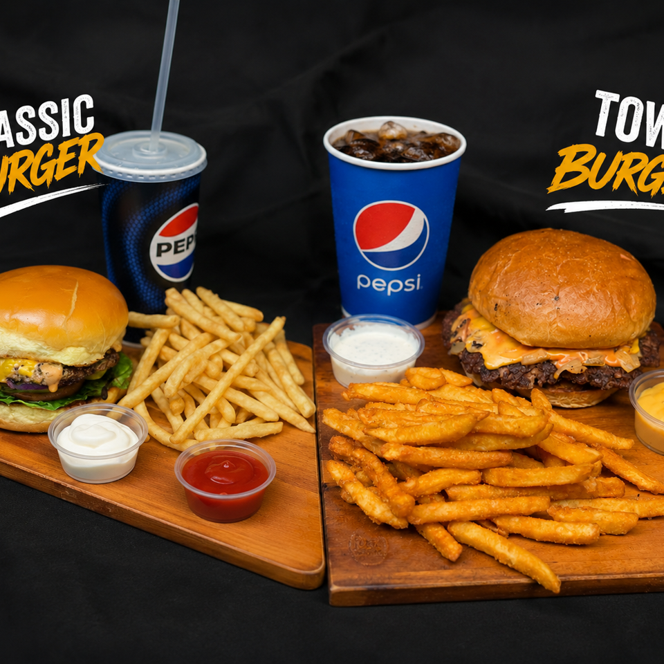 Classic and town cheeseburgers with fries, dipping sauces, and Pepsi drinks arranged on wooden boards against a black background.