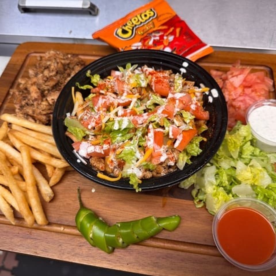 Loaded Middle Eastern-style platter with seasoned meat, fries, chopped salad, pickled onions, jalapeños, sauces, and a bag of Cheetos.